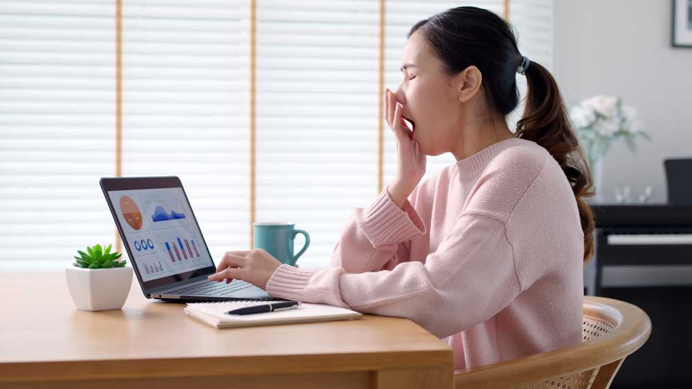 Woman yawning at desk with laptop - representing inconsistent follow-up